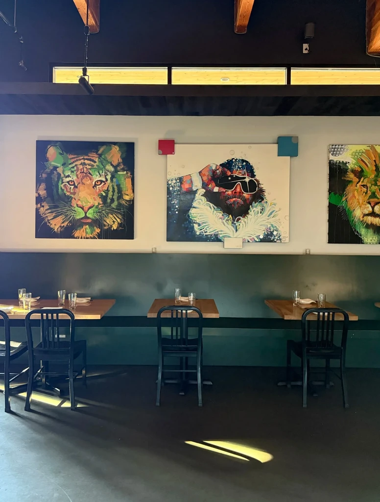 Restaurant dining area with pop-art tiger, Randy Savage, and lion paintings.