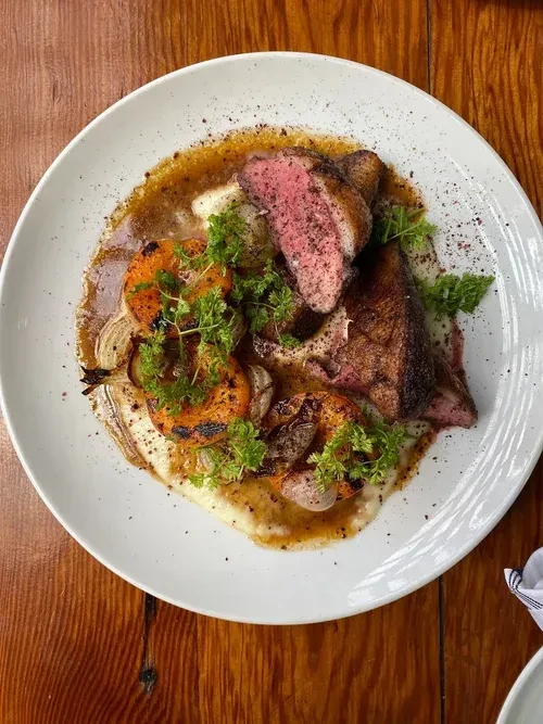 Top-down: Seared meat, creamy purée, roasted vegetables, and brown sauce.