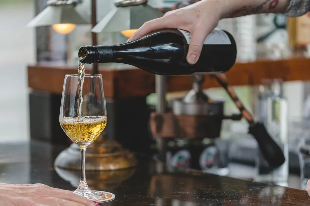 Hand pouring white wine into a stemmed glass at a bar.