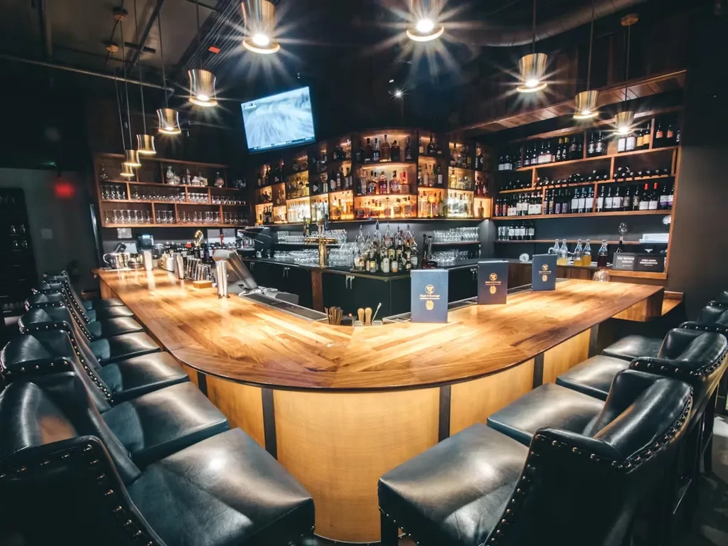 Elegant, empty restaurant bar with polished wooden counter and backlit liquor.