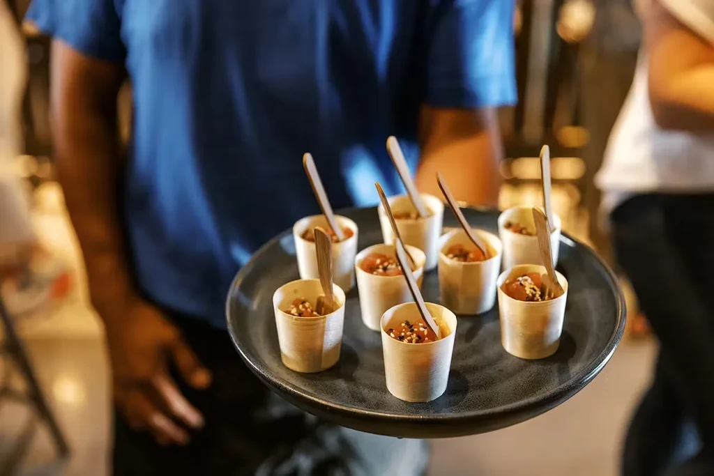 Person holds tray of eight wooden cups with food and spoons.