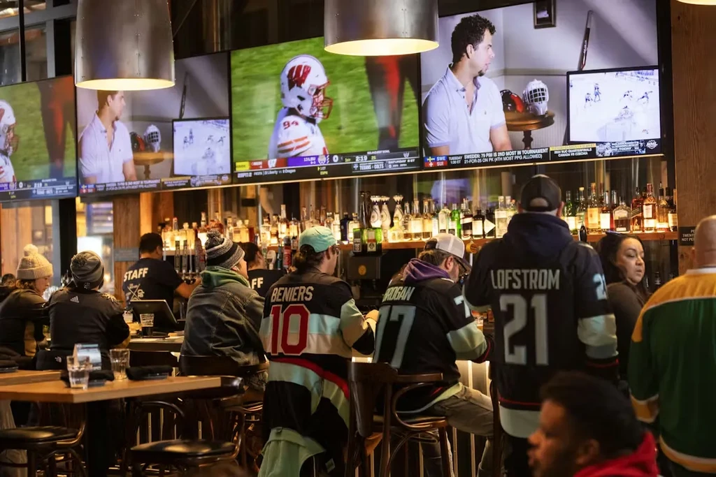 Sports bar interior: multiple TVs above a stocked bar, with patrons.