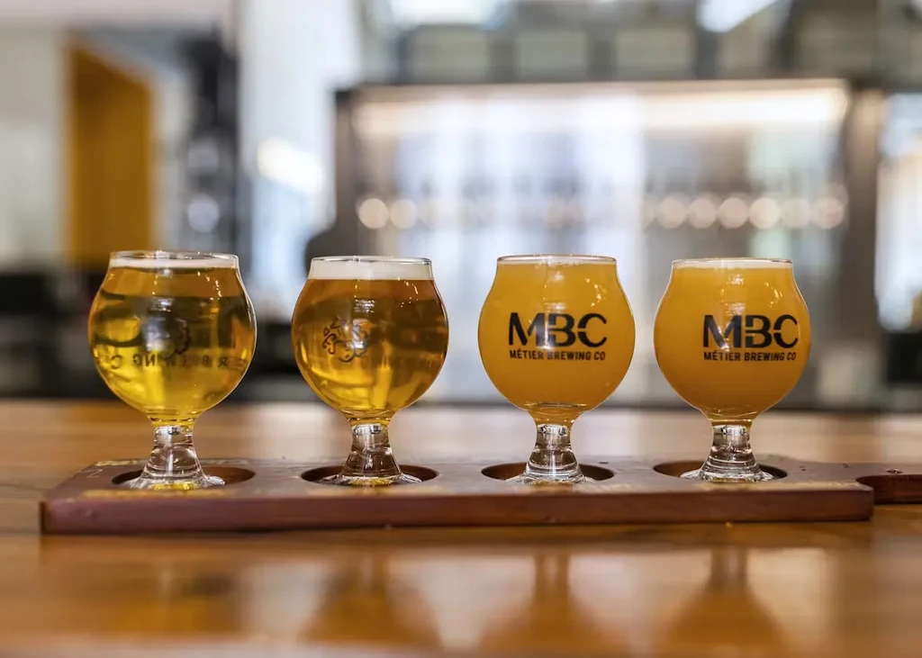Four glasses of light and hazy beer on a wooden paddle.