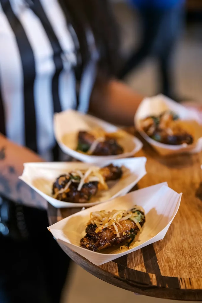 Glazed chicken wings with shredded garnish in wooden boat dishes.