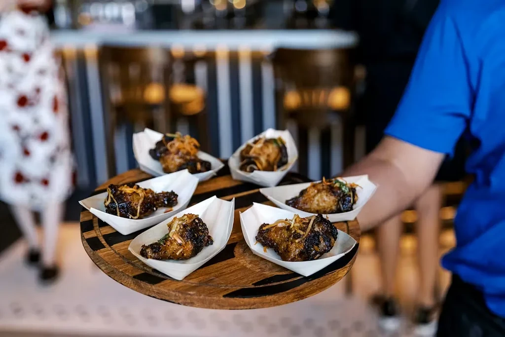 Person holding a round wooden platter of six glazed chicken wings.
