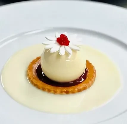 Plated dessert: spherical white mousse on tartlet with flower decoration and sauce.