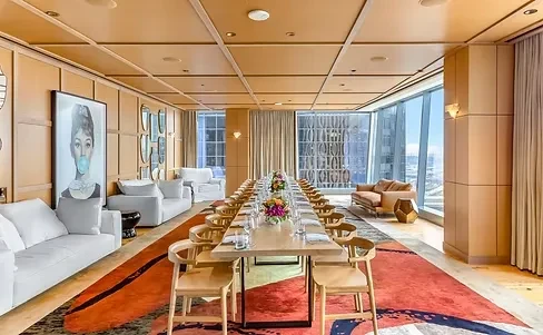 Modern dining room with city view, long table, lounge area, and artwork.