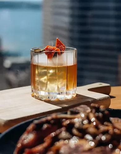 Amber smoky cocktail with dried fruit, blurred city view.