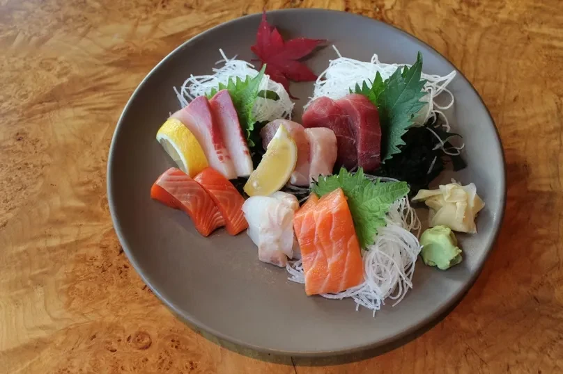Plate of assorted sashimi with garnishes and a red maple leaf.