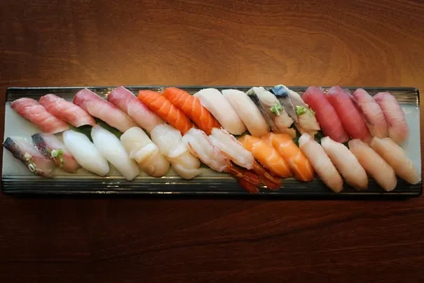 Two rows of diverse, colorful nigiri sushi on a dark platter.