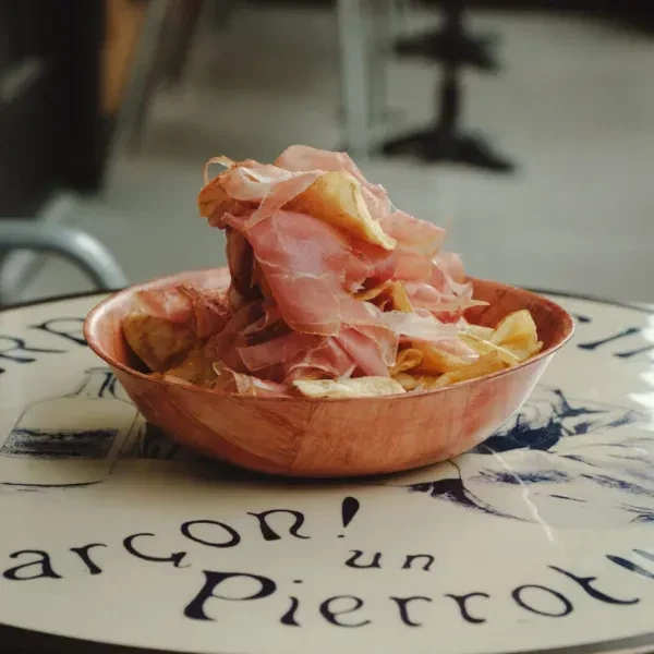 Rustic bowl of potato chips and cured meat on a bistro table.