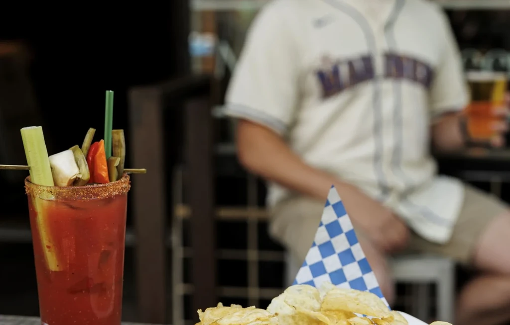 Garnished Bloody Mary, chili salt rim, chips, and a person holding beer.