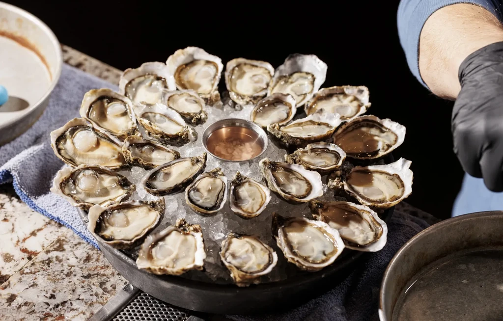 Platter of fresh shucked oysters on ice with dipping sauce.