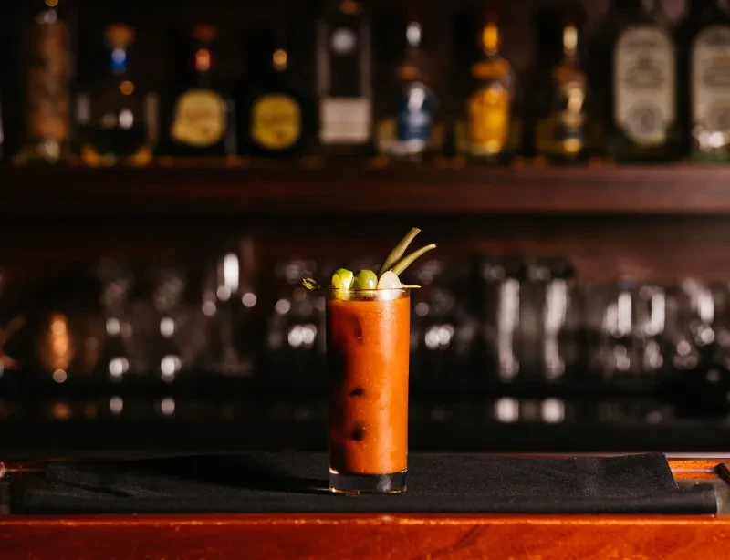 Garnished Bloody Mary cocktail on a dimly lit wooden bar.