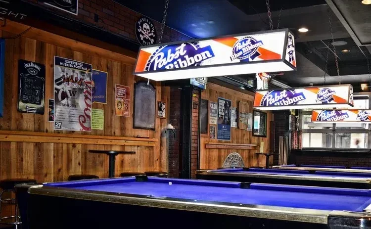 Blue felt pool tables in a bar under Pabst Blue Ribbon lights.