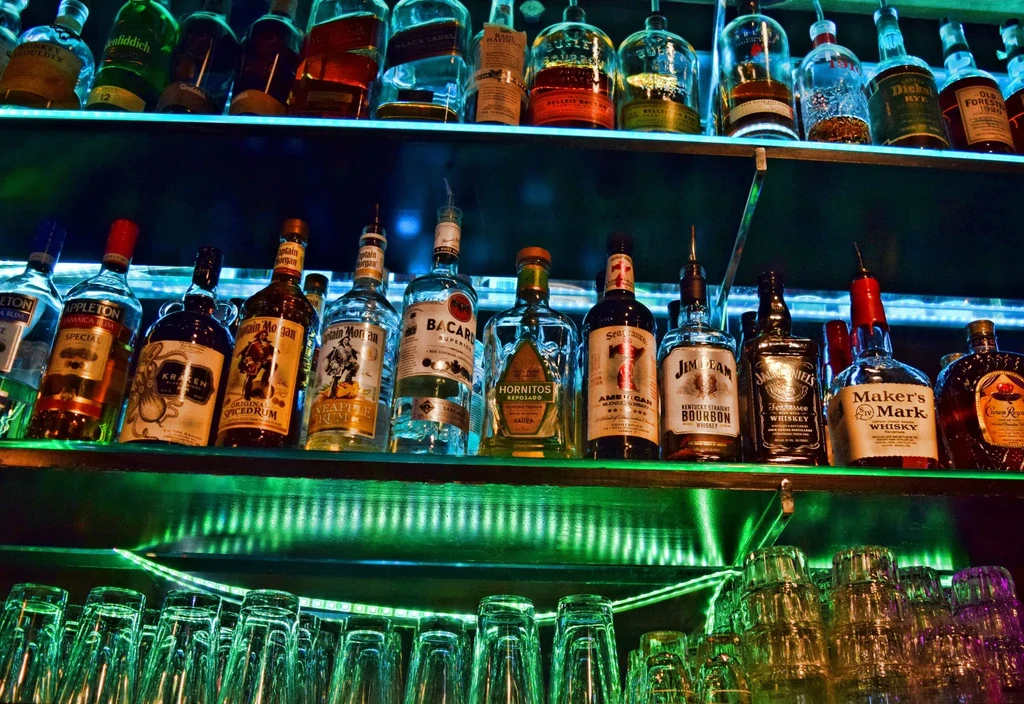 Bar shelves with liquor bottles and glassware, lit by green and blue LEDs.
