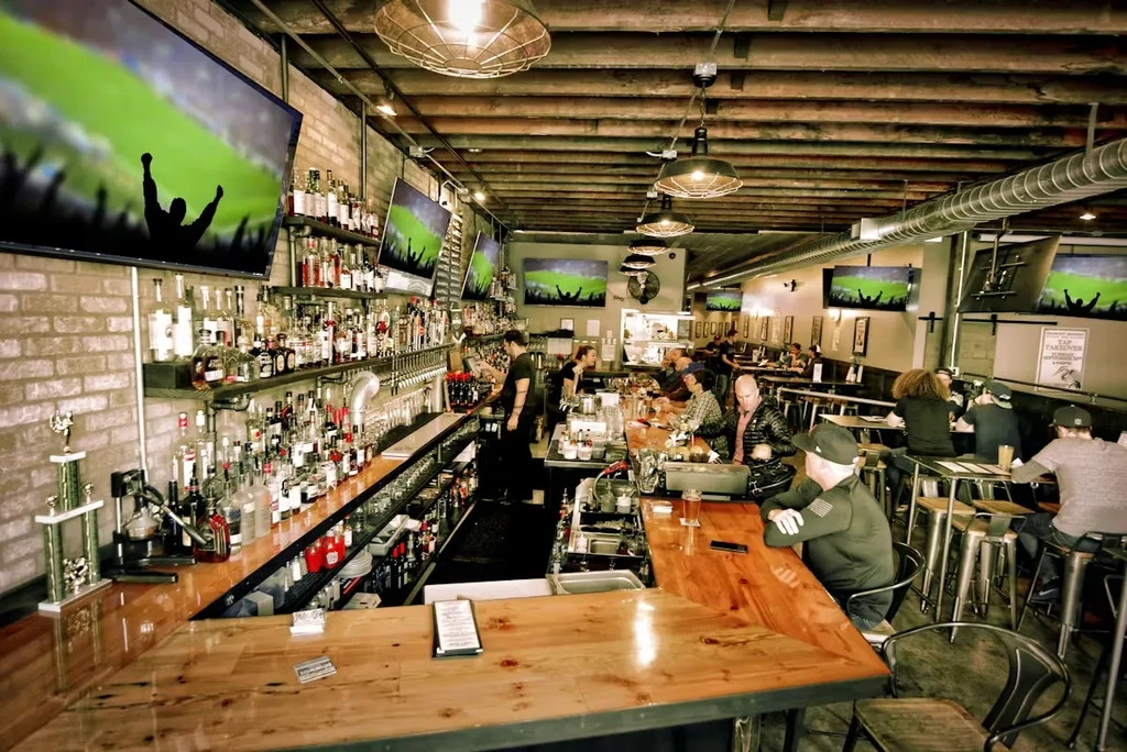 Lively industrial-style bar with exposed brick, sports on TV, and patrons.