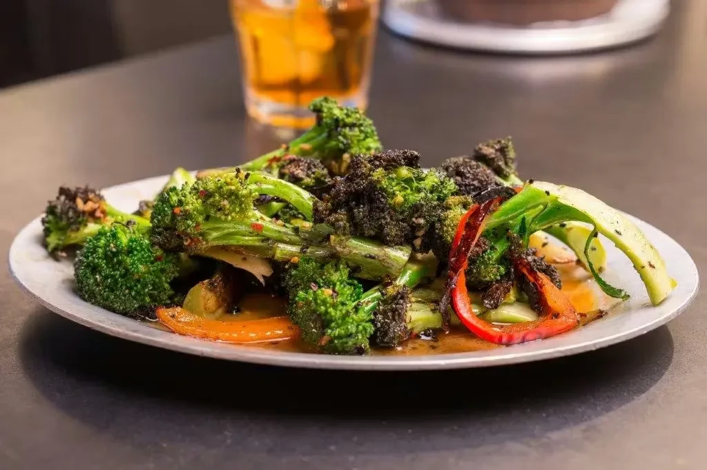 Plate of roasted broccoli, red bell peppers, zucchini, and sesame seeds.