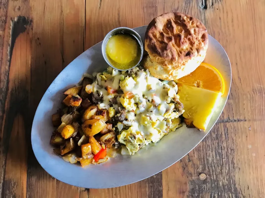 Overhead of hearty breakfast plate: eggs, potatoes, biscuit, fruit.