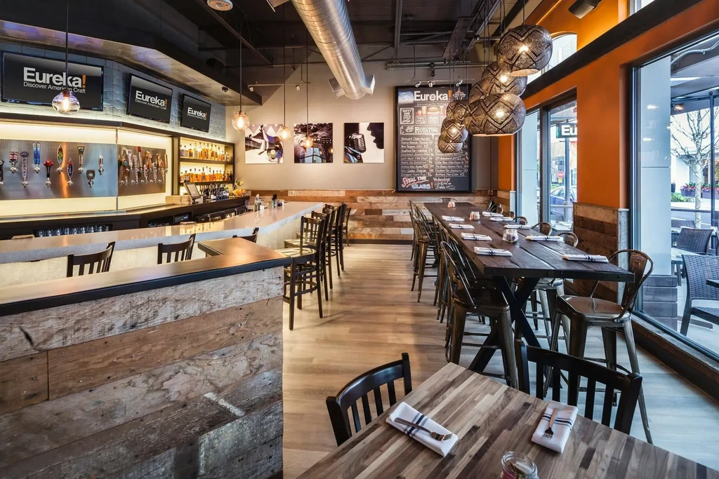 Empty modern industrial-chic restaurant interior with a prominent bar and diverse seating.