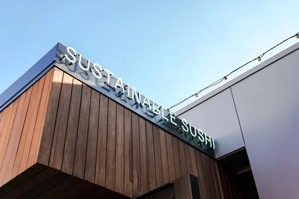 Modern building, "SUSTAINABLE SUSHI" neon sign, wood and grey facade.