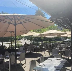 Large beige umbrellas shade an outdoor dining patio on a sunny day.