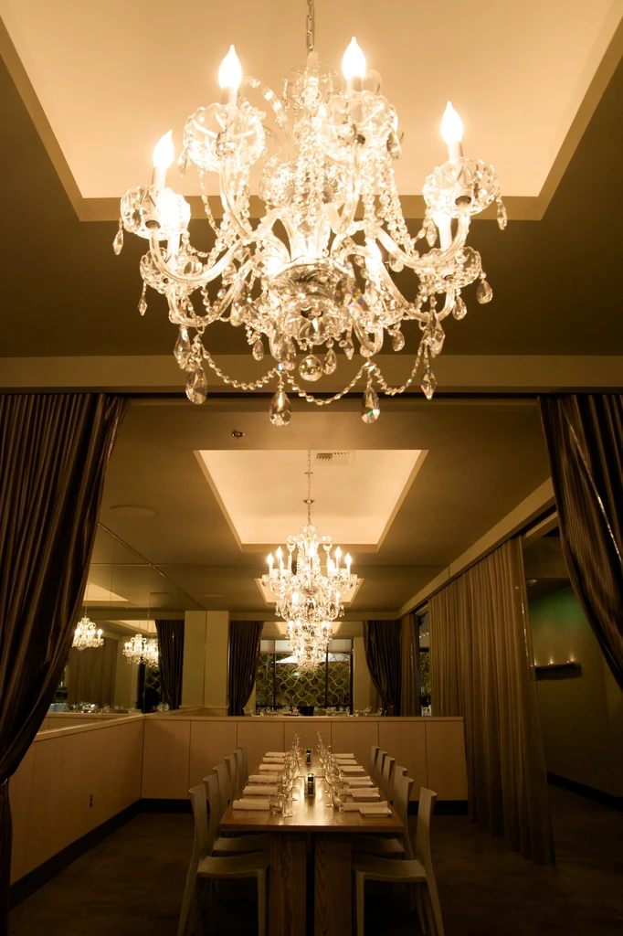 Elaborate crystal chandeliers illuminate an elegant dining room and set table.