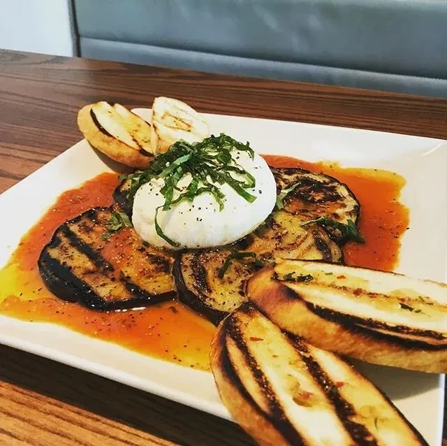 Grilled eggplant with burrata, herbs, tomato sauce, and grilled bread.
