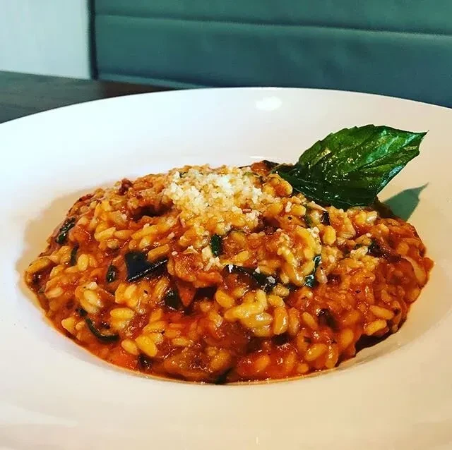 Top-down view of tomato risotto with grated cheese and basil.