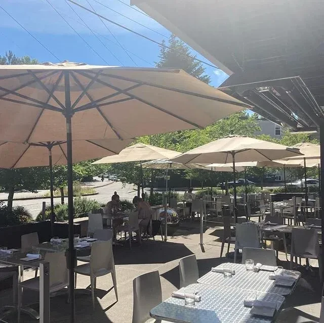 Sunny outdoor dining patio with set tables and open umbrellas.