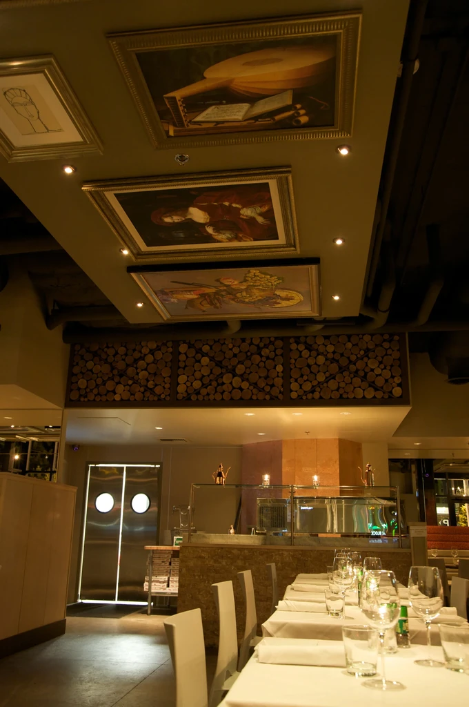 Dimly lit, sophisticated restaurant with ceiling art and set tables.