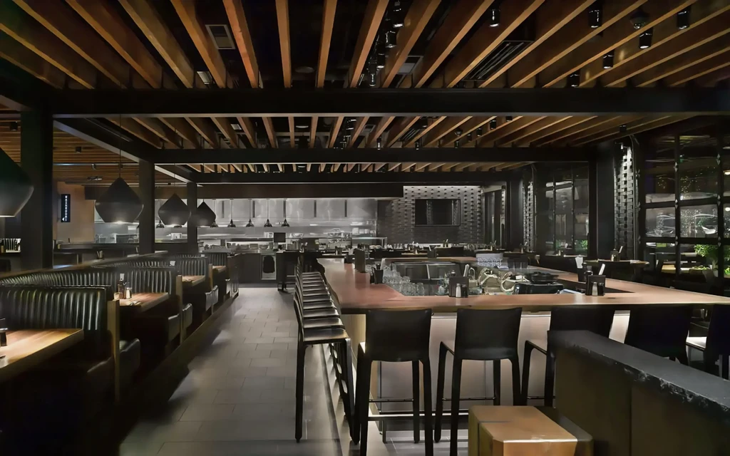 Modern restaurant interior with dark booths, wooden bar, and open kitchen.
