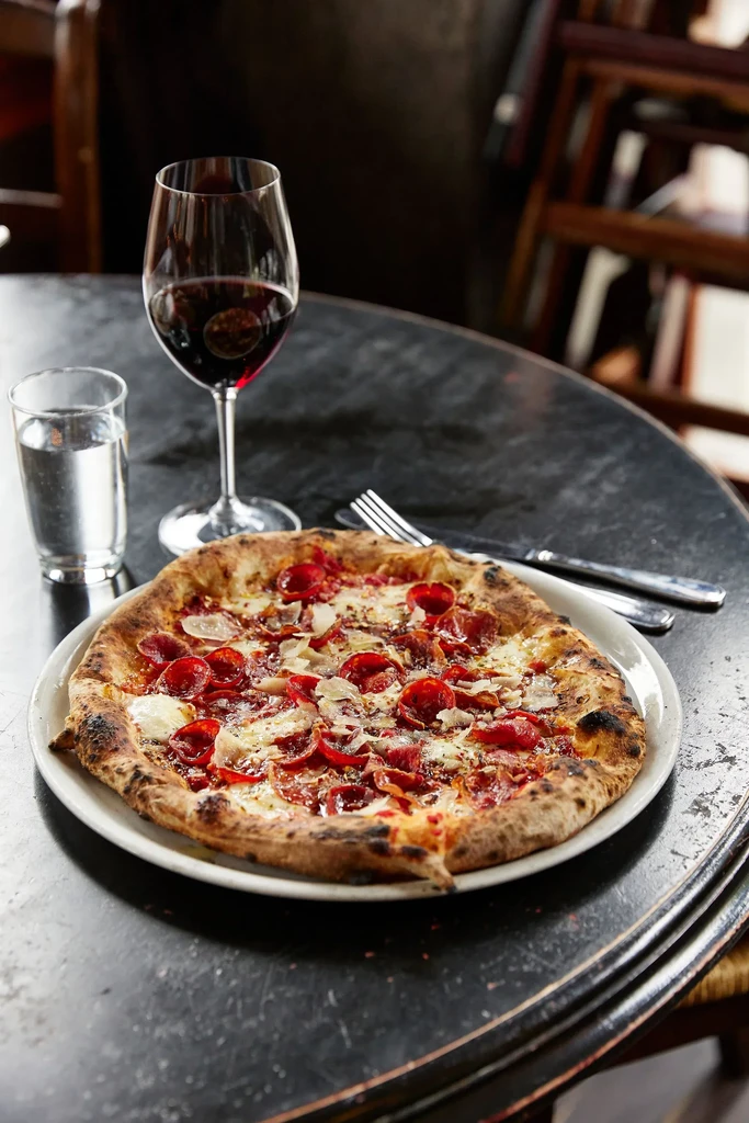 Close-up pepperoni pizza, red wine, and water on a dark table.