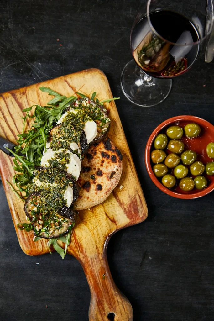 Top-down view of grilled eggplant, cheese, flatbread, wine, and olives.