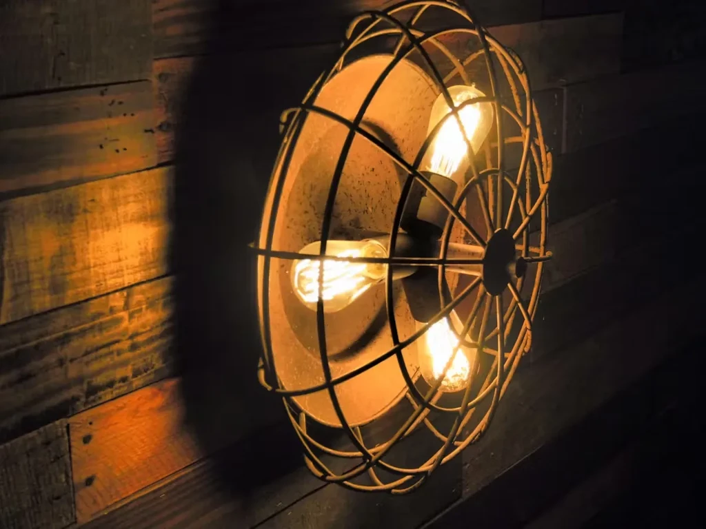 Distressed industrial wall light with three glowing Edison bulbs on wood.