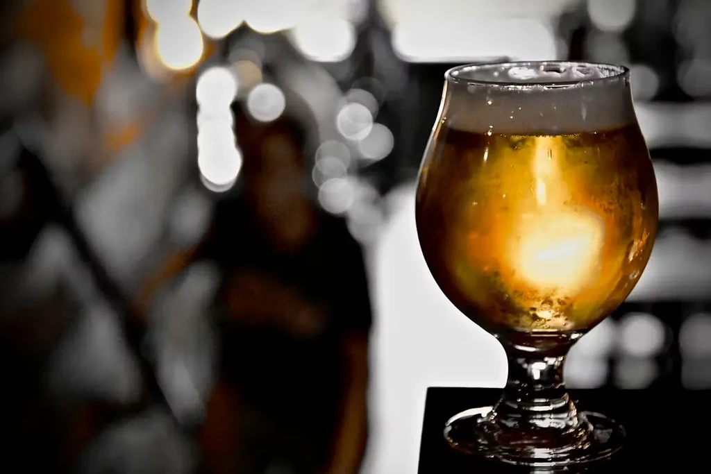 Stemmed glass of golden beer with foam, blurred bar background.