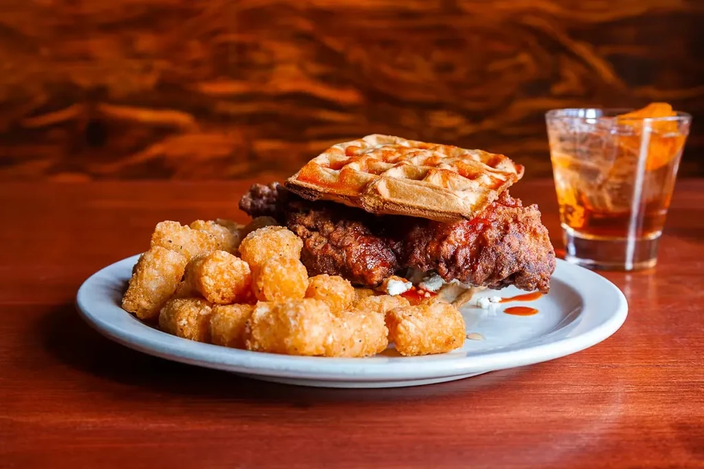 Close-up of chicken and waffles, tater tots, and an amber drink.
