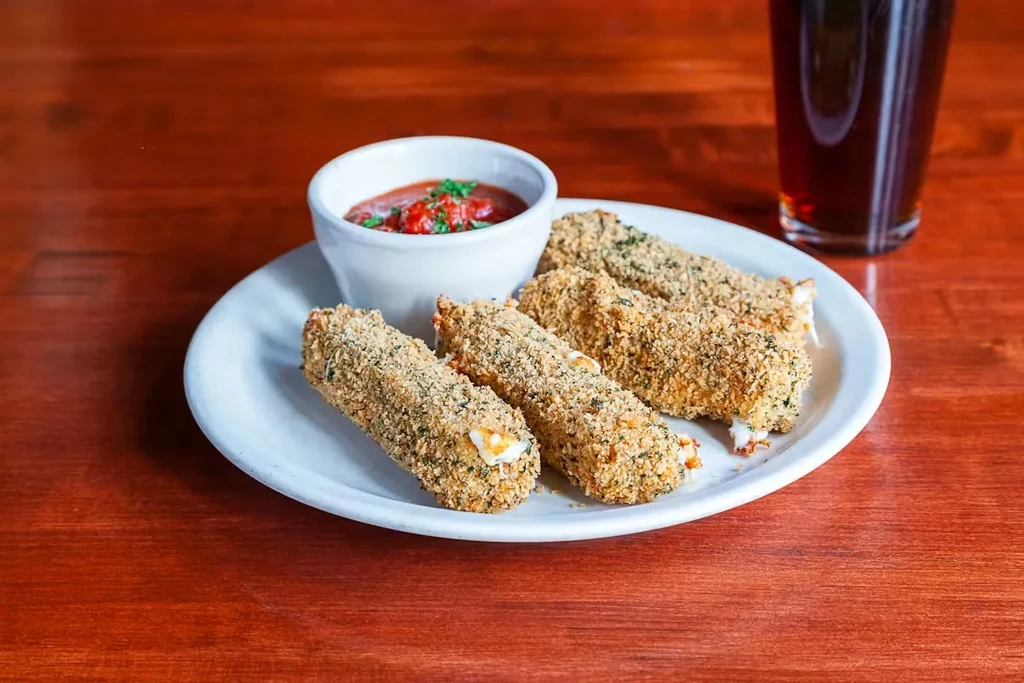 Mozzarella sticks with marinara, a dark drink, on a wooden table.