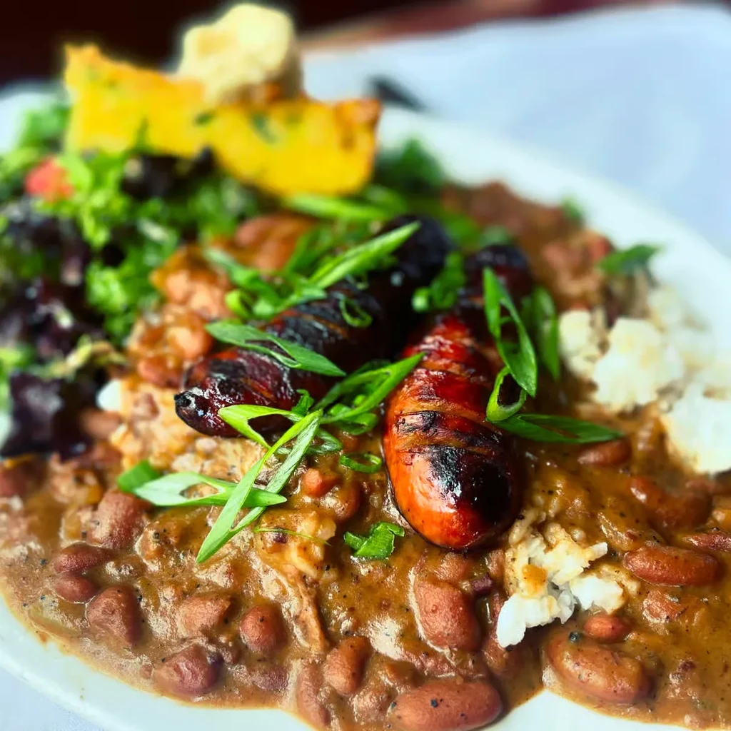 Close-up of red beans and rice with grilled sausage, salad, and cornbread.