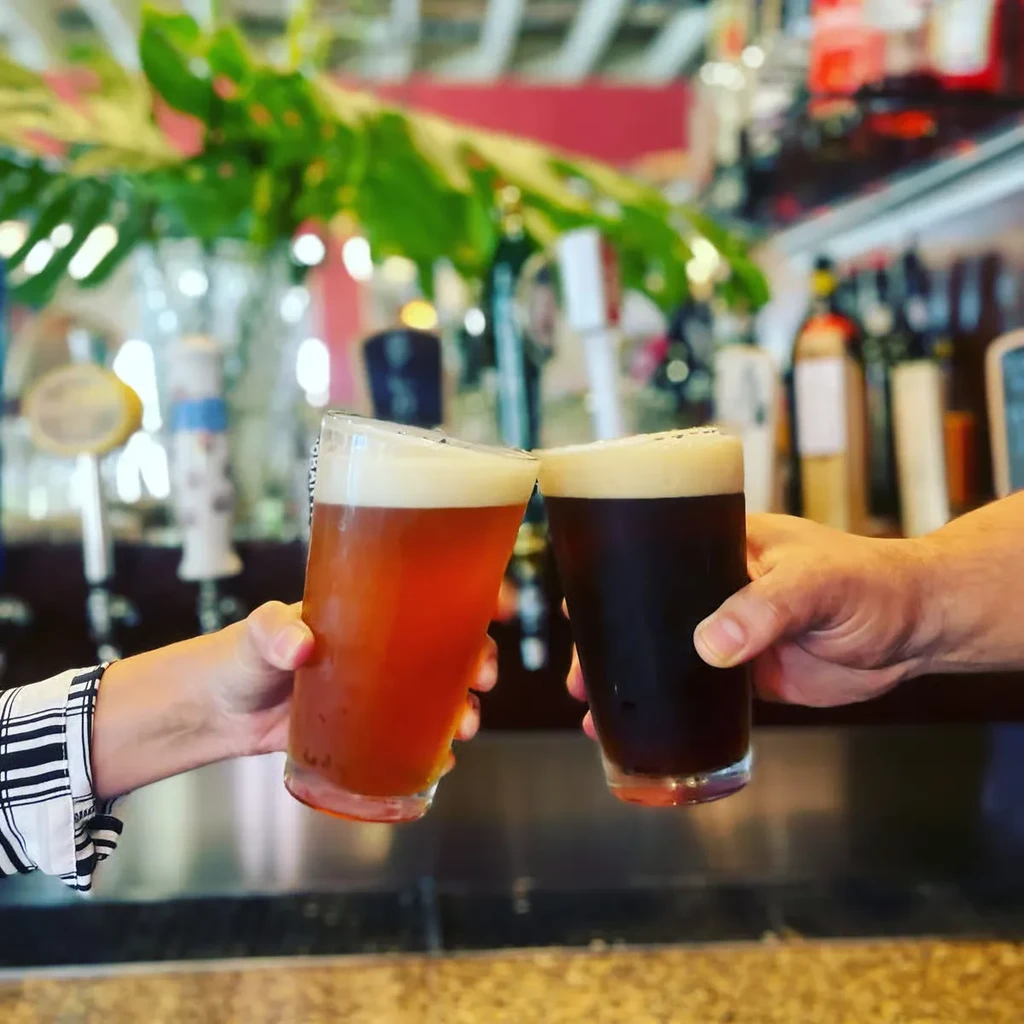 Two hands clinking amber and dark beers at a bar.