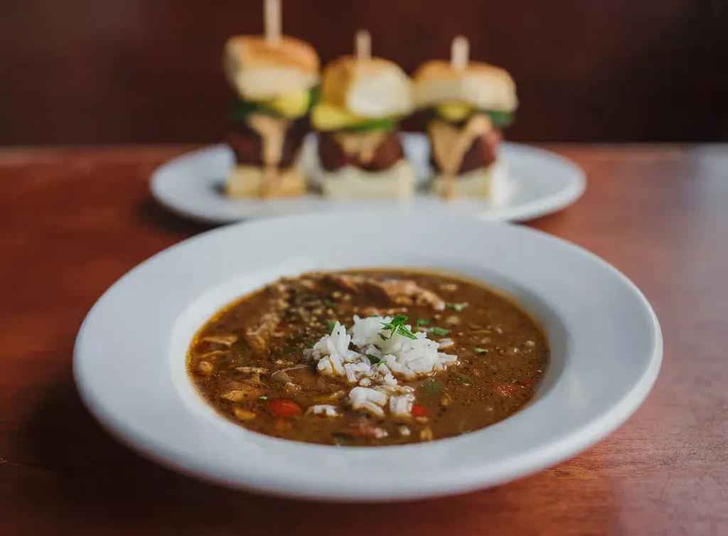 Dark stew with rice in a bowl; blurred sliders on a plate.