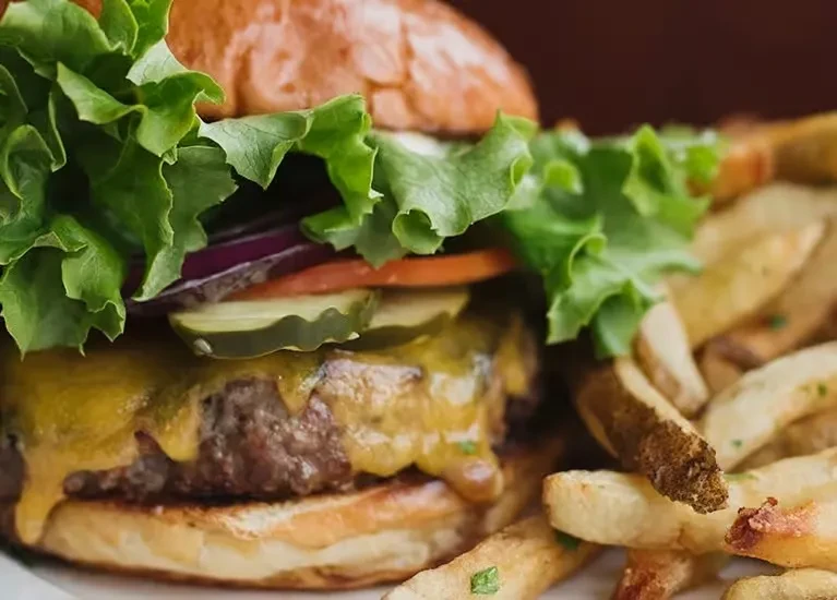 Close-up of a gourmet cheeseburger and herb-seasoned potato wedges.