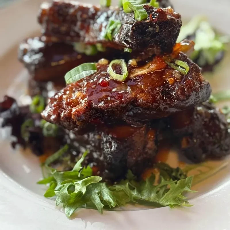 Stacked glazed short ribs garnished with green onions and lettuce.
