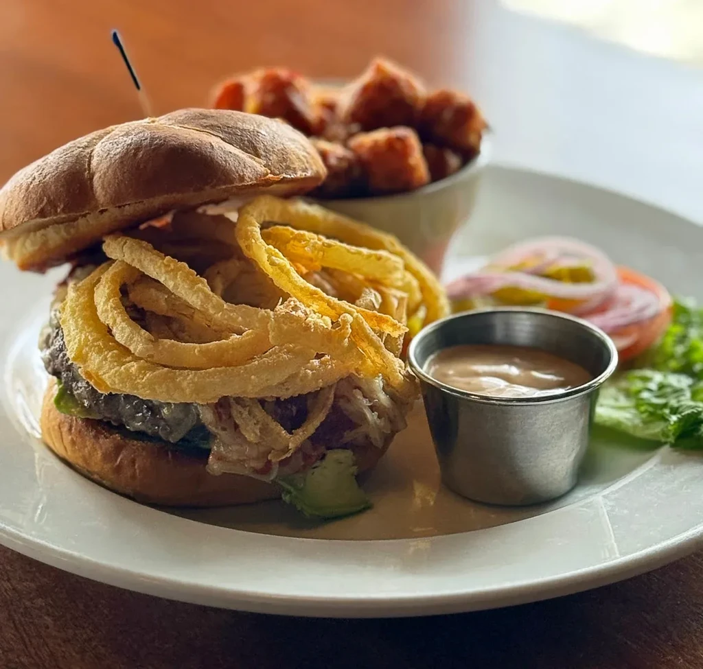 Gourmet burger with onion rings, creamy sauce, and fresh garnishes.