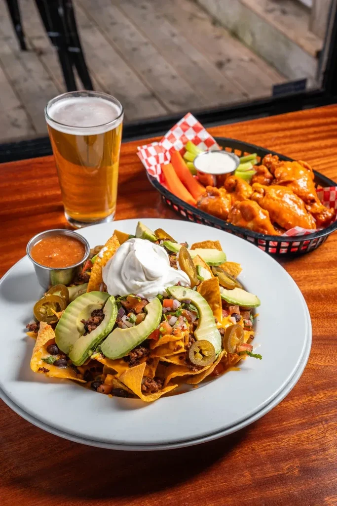 Loaded nachos, beer, and buffalo wings on a wooden table.
