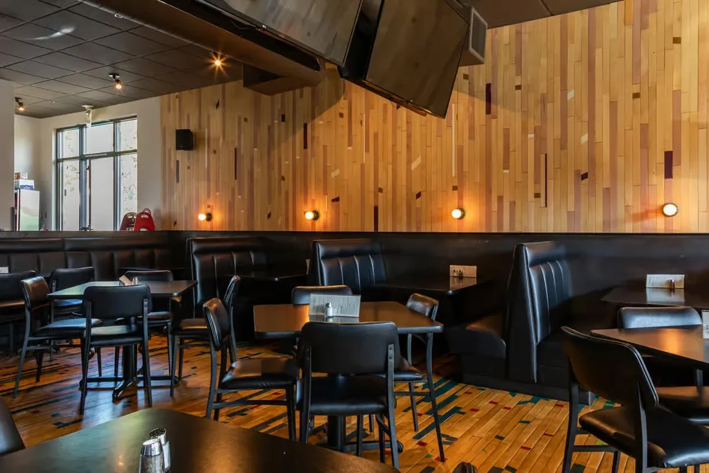 Modern restaurant interior with black booths, wood walls, and colorful patterned floor.