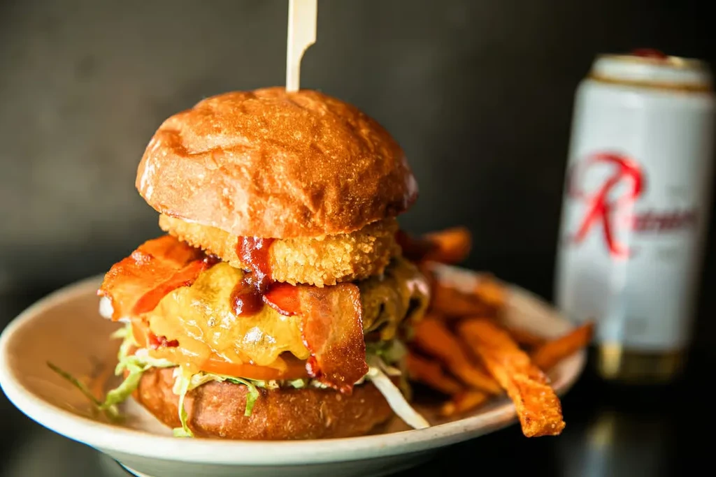 Gourmet burger with bacon, onion rings, and sweet potato fries.