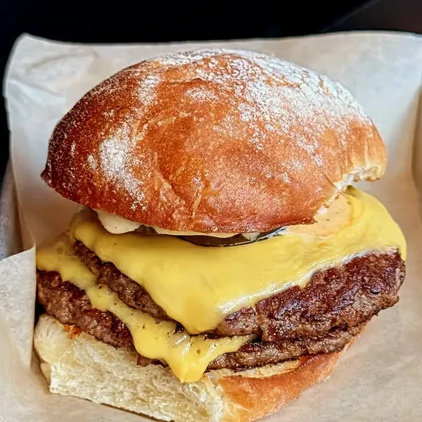Close-up double cheeseburger with melted cheese, creamy sauce, and a dusted bun.
