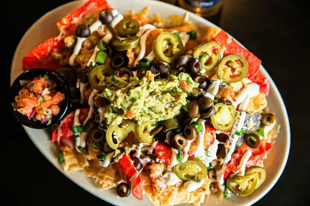 Overhead view of nachos topped with guacamole, jalapeños, sour cream, and salsa.