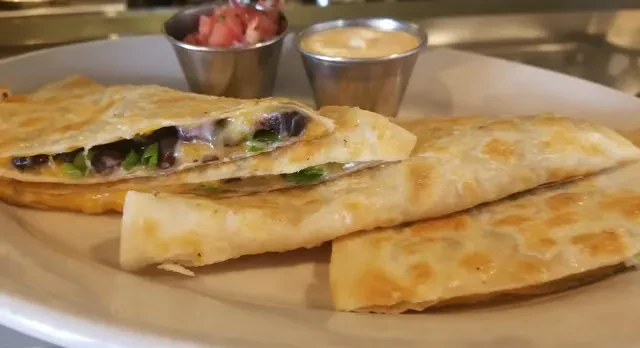 Three quesadilla wedges, filled with cheese and beans, with two dips.
